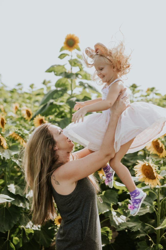 mom catches daughter and daughter's pink dress poofs up into air and over mom's face in sunflower pictures at tuttle orchard