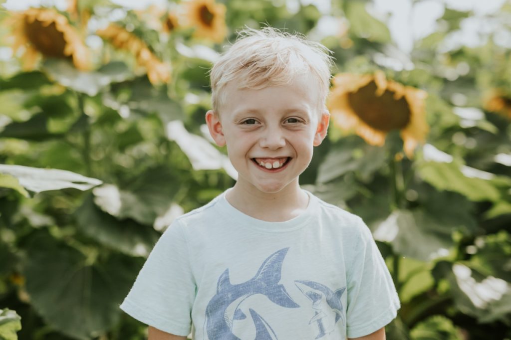 a young blonde boy smiles in sunflower pictures at tuttle orchard