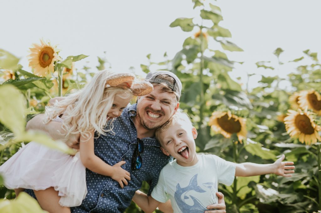 goofy kids attack their dad with hugs in sunflower pictures at tuttle orchard