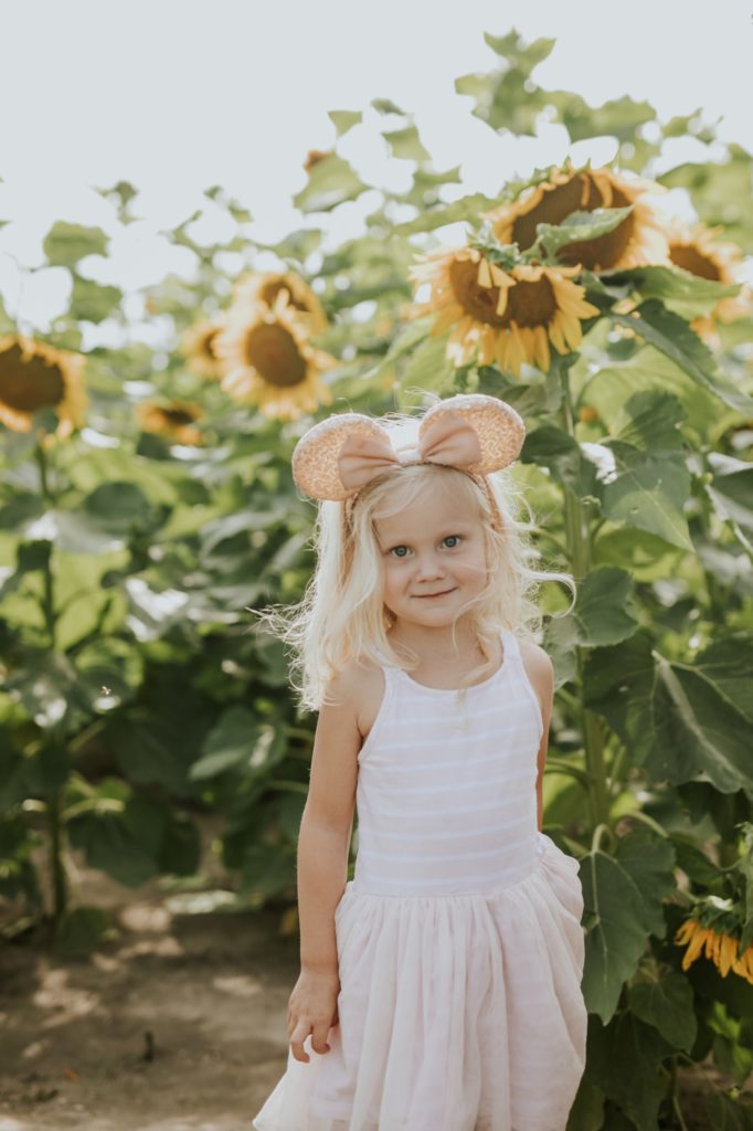 girl in dress smiles in yellow flower field while wearing minnie mouse ears