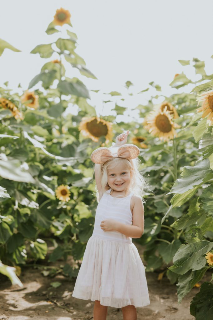 small blonde girl in minnie ears smiles and plays with flowers at tuttle orchard