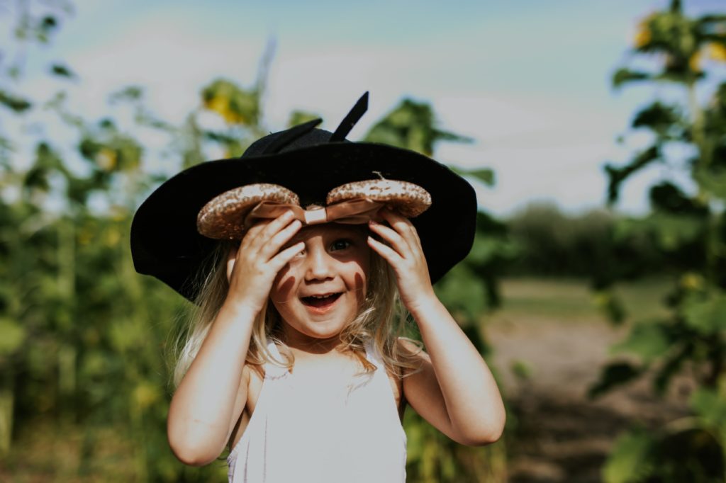 blonde daughter puts on mom's hat and smiles in sunflower pictures at tuttle orchard
