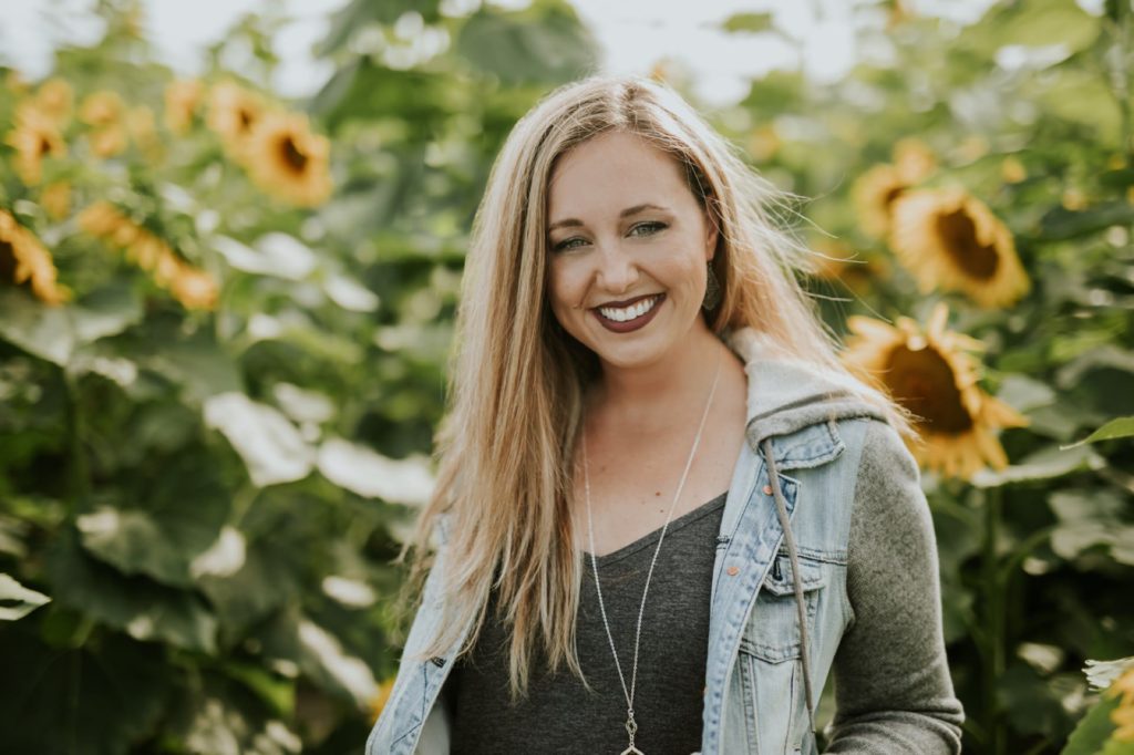 pretty woman with brown hair smiles in a flower field in indianapolis while wearing a jean jacket