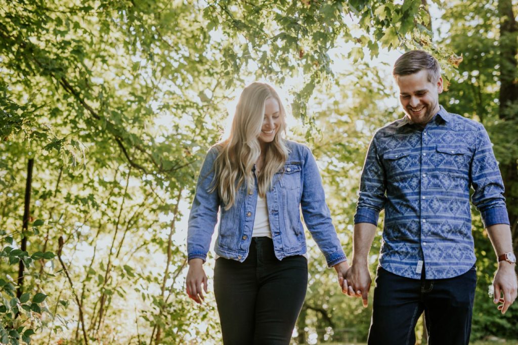 a brown-haired man and blonde woman hold hands and walk through a forest at an Indianapolis park