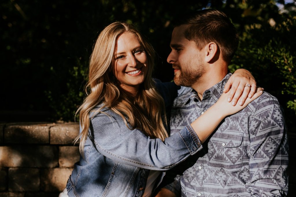 a blonde woman hugs a man in a dark and moody engagement portrait in indianapolis