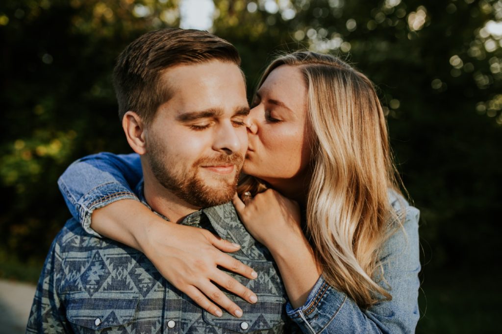 a blonde woman kisses a man on the cheek in the woods during their Eagle Creek Engagement Photos