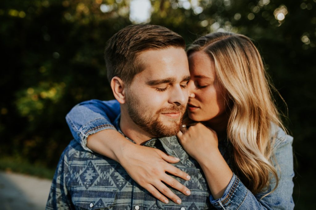 a woman hugs a man from behind and rests her forehead against the man during their Eagle Creek Engagement Photos