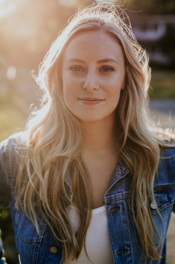 a blonde woman backlit by the sun looks at the camera during her Eagle Creek Engagement Photos
