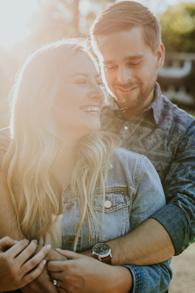 a man hugs a woman from behind and they both smile during their Eagle Creek Engagement Photos