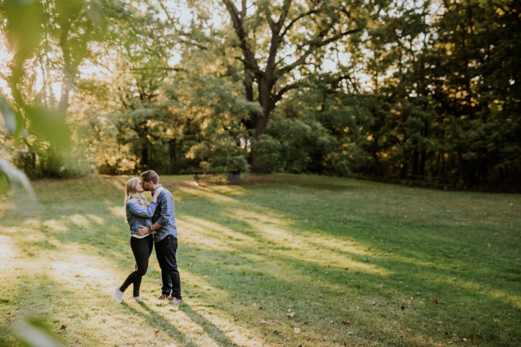 a man and woman hug in a field of grass at sunset during their indy park engagement session