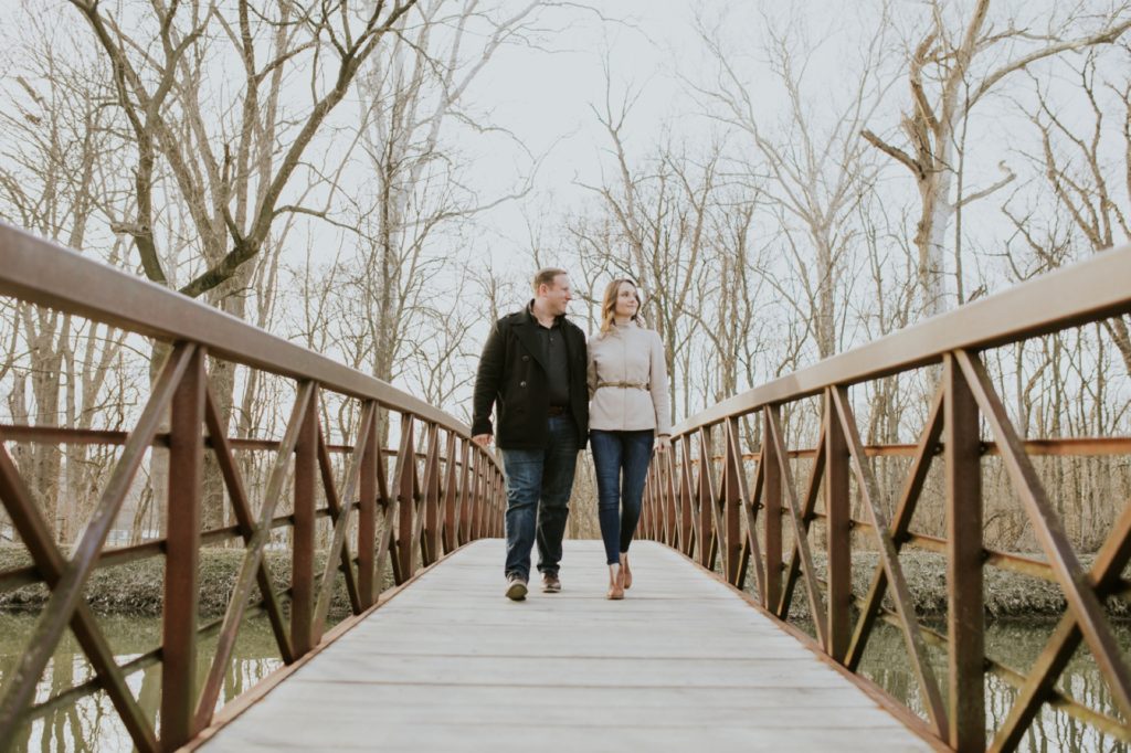a man and a woman walk across a bridge in fall weather for their butler university portrait session