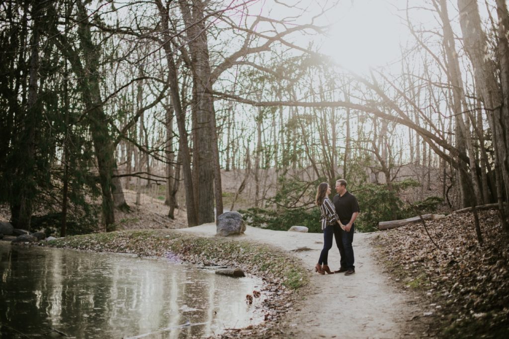 a man and a woman stand under a tree at sunset during their butler university portrait session