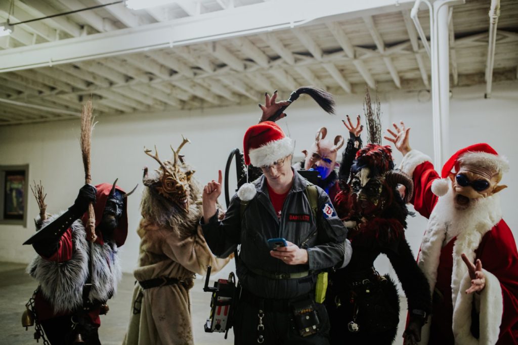 ghostbuster checks phone and holds up finger so krampus will wait to attack him at scarlet lane at this herst with scarlet lane brewing company logo on back at this Indianapolis Brewery Event Photography