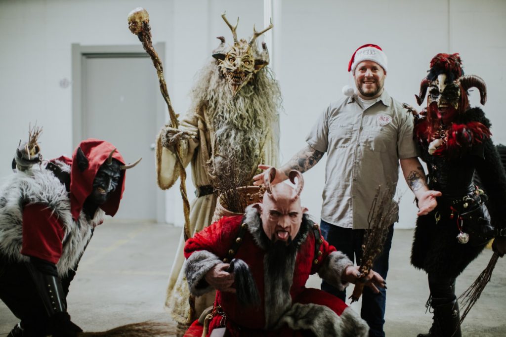 director josh hull in santa hat and scarlet lane shirt poses for photo with several krampus at this herst with scarlet lane brewing company logo on back at this Indianapolis Brewery Event Photography