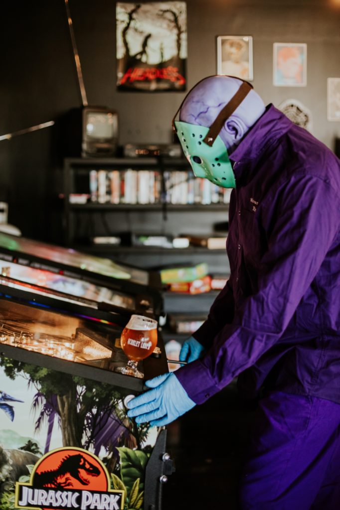 man in purple jumpsuit with purple skin and hockey mask plays jurassic park pinball at scarlet lane