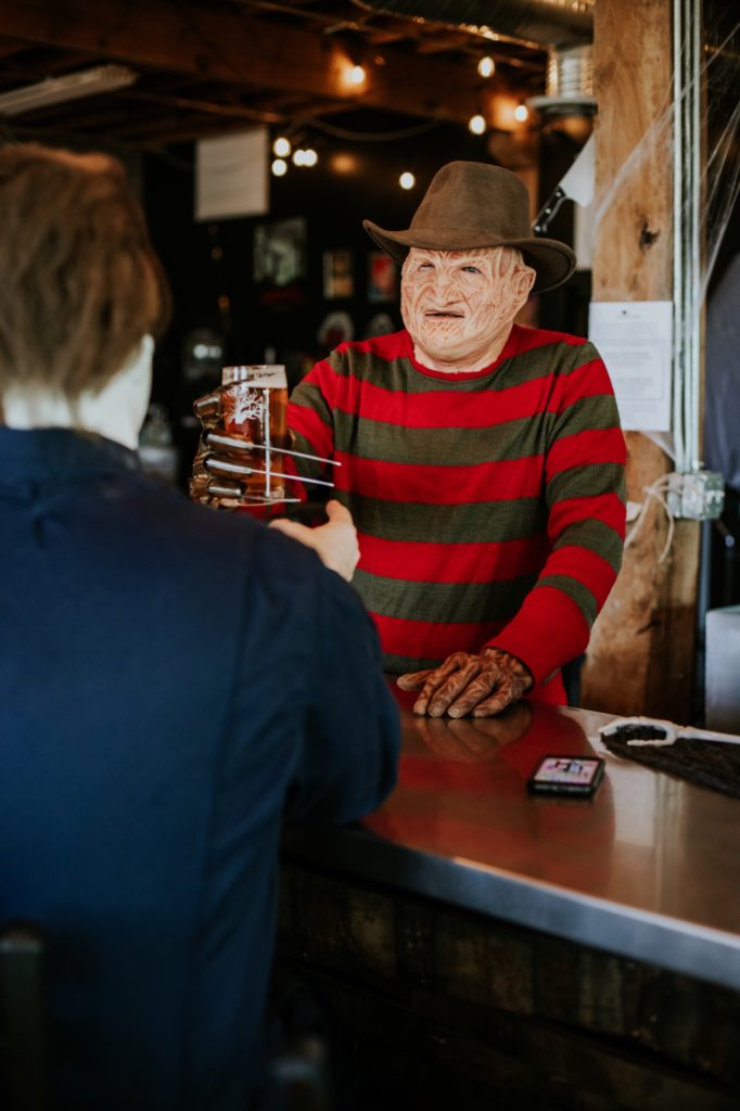 stripey man with scarred face clinks beer with someone with his clawed hand at scarlet lane brewery in this Indianapolis brewery photography