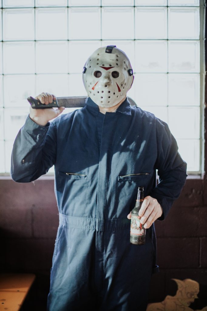 hockey mask guy holds machete and beer in front of window