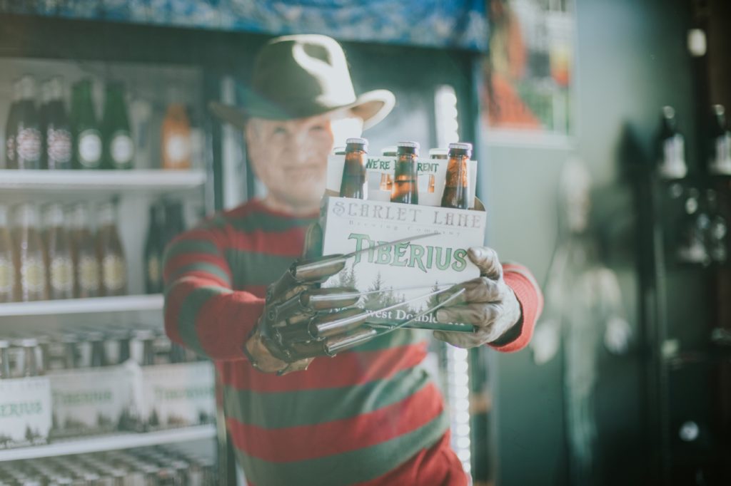 stripey shirt guy with claw hand holds tiberius beer six pack in front of him in this Indianapolis brewery photography