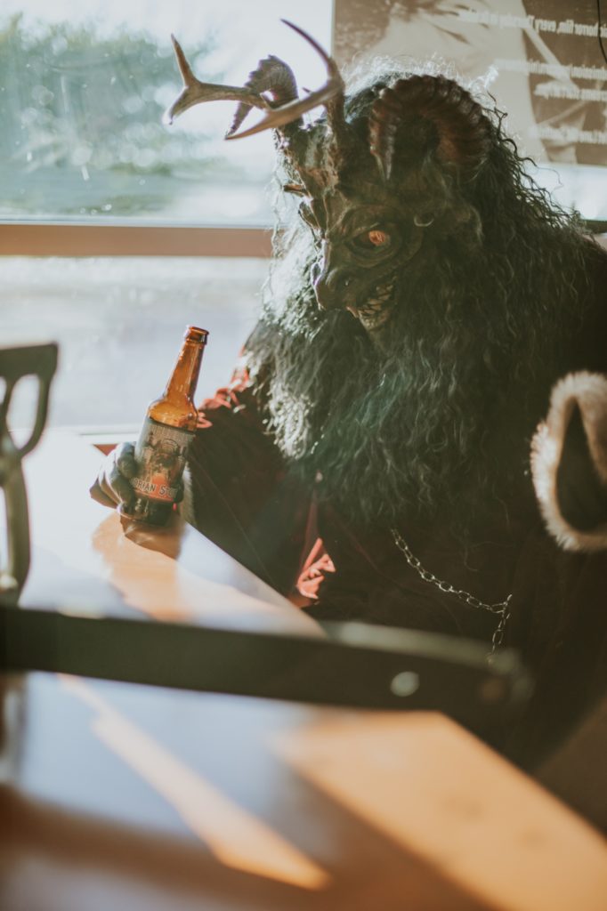 man in krampus mask pounds a bottle of beer