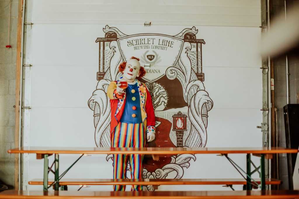 clown holds beer and stands in front of scarlet lane logo for this Indianapolis brewery photography