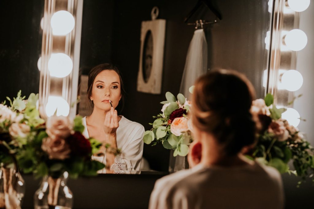 bride applies lipstick while looking in mirror at industrial wedding venue