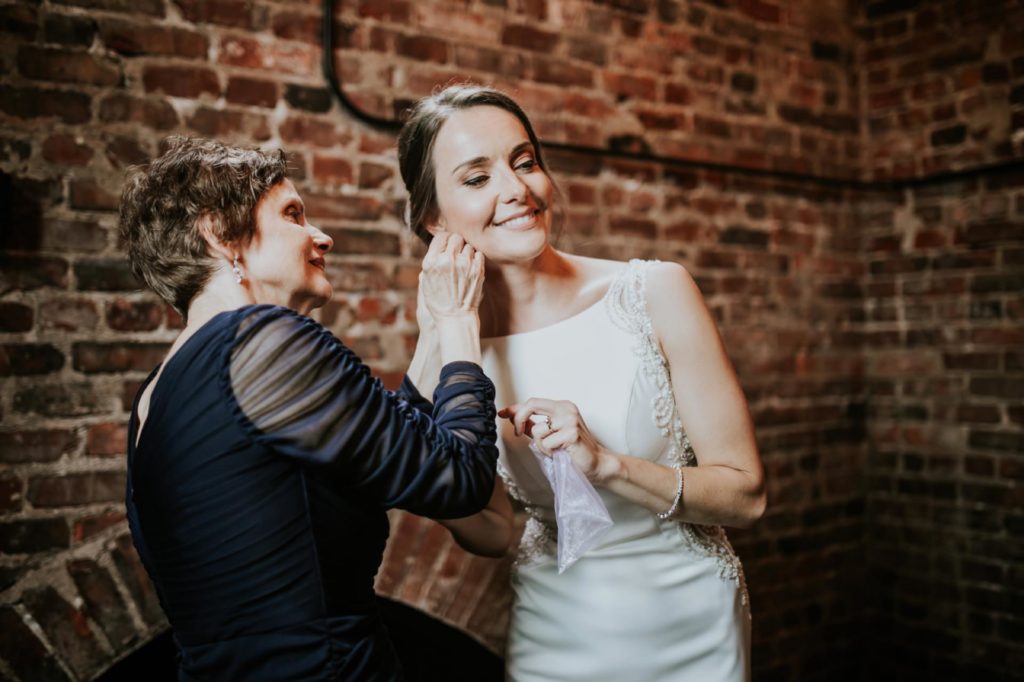mother of bride helps bride put in her earrings at a canal 337 wedding