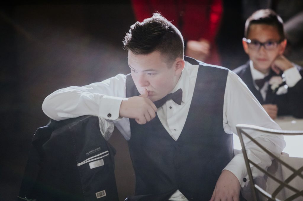 a teenage boy in a tux looks down while resting his chin on his hand
