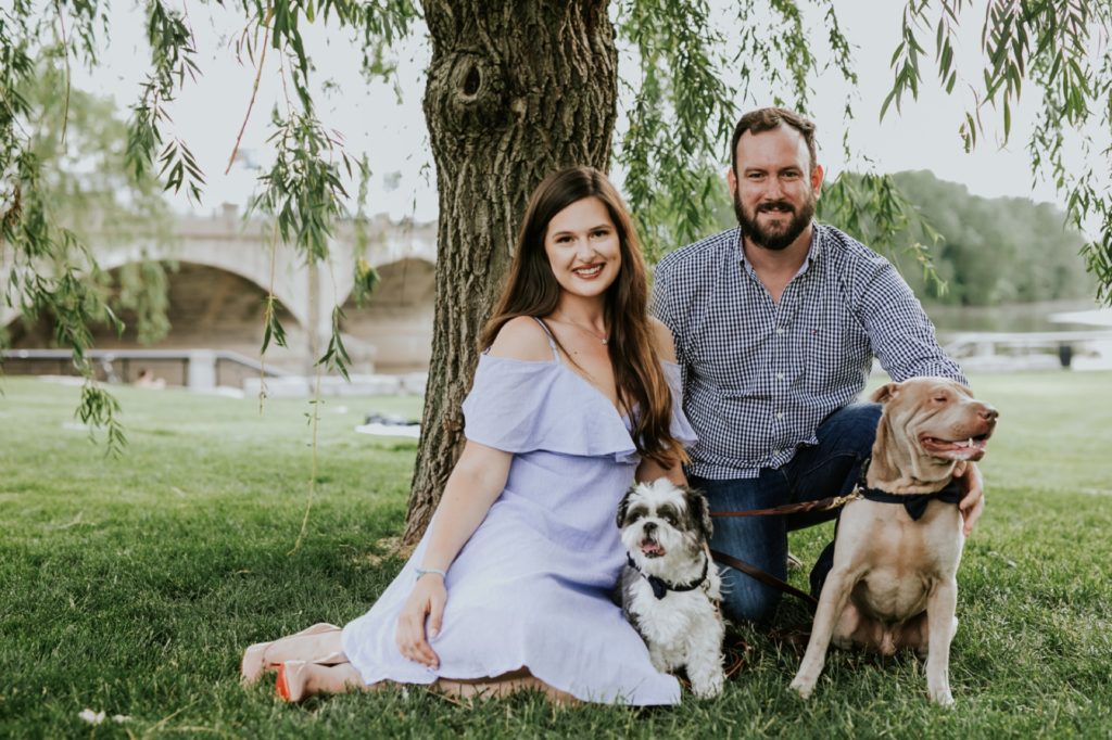 man and woman sit under tree with two dogs for white river state park engagement picture