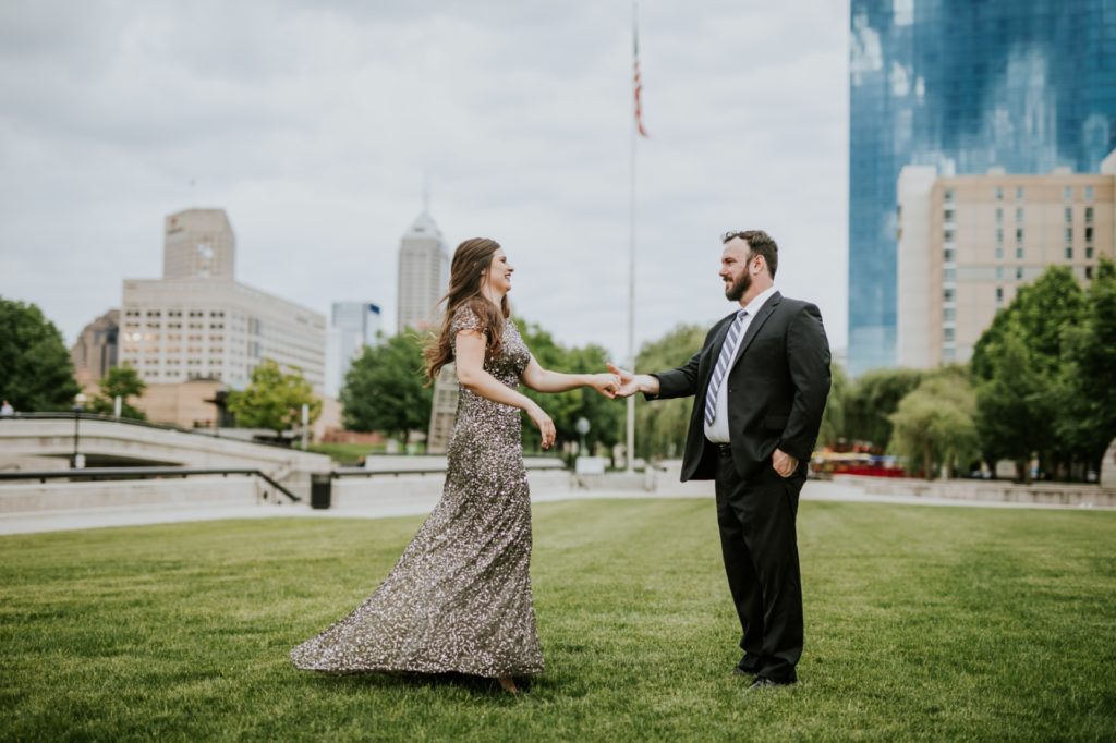 woman in floor length ball gown dances on grass with man in suit in white river state park engagement picture