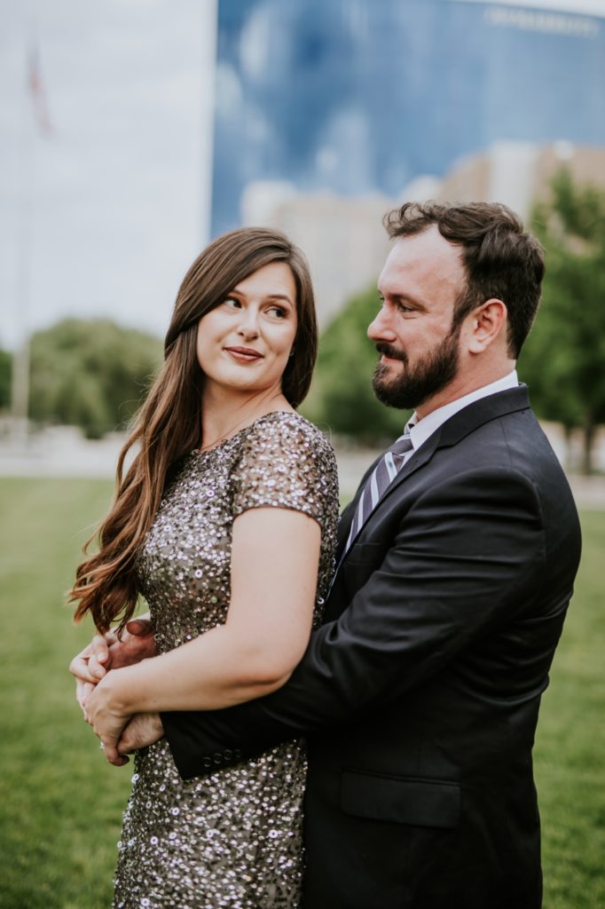 bearded man in suit hugs woman in sequenced ball gown on grass in white river state park engagement picture