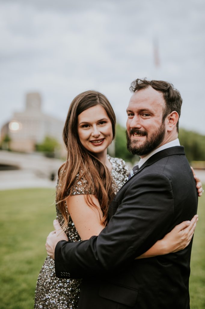 bearded man in suit hugs woman in gold sequence ball gown in white river state park engagement picture