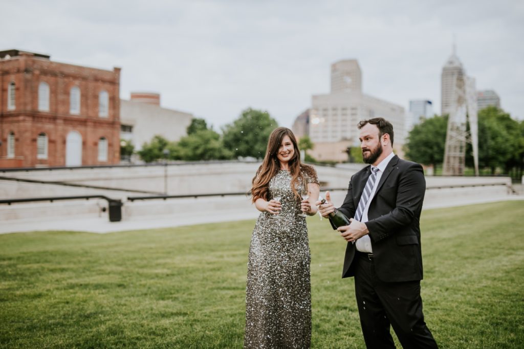 man and woman in formal wear pop a bottle of champagne in white river state park engagement picture