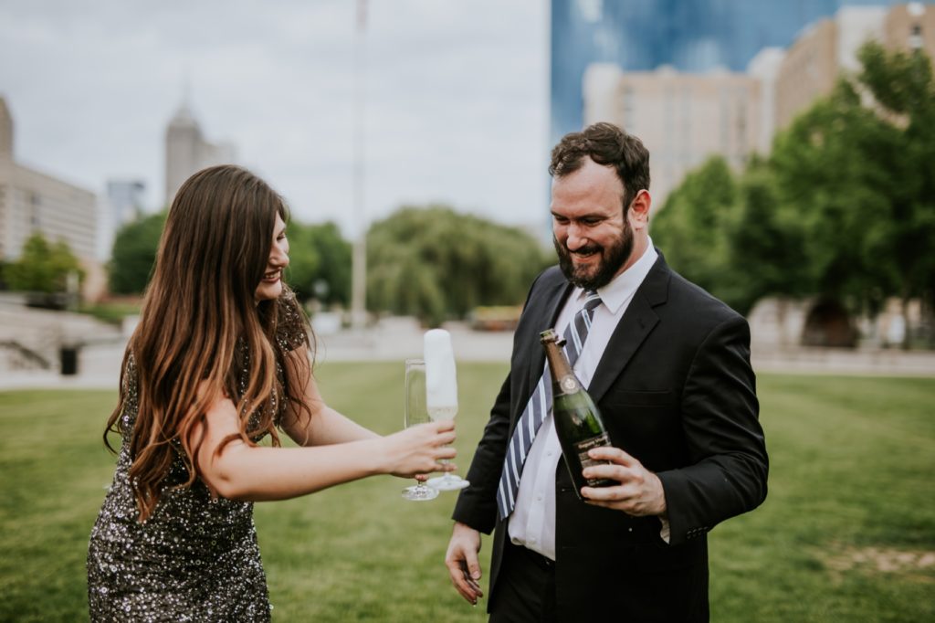 man and woman in formal clothes drink champagne in white river state park engagement picture