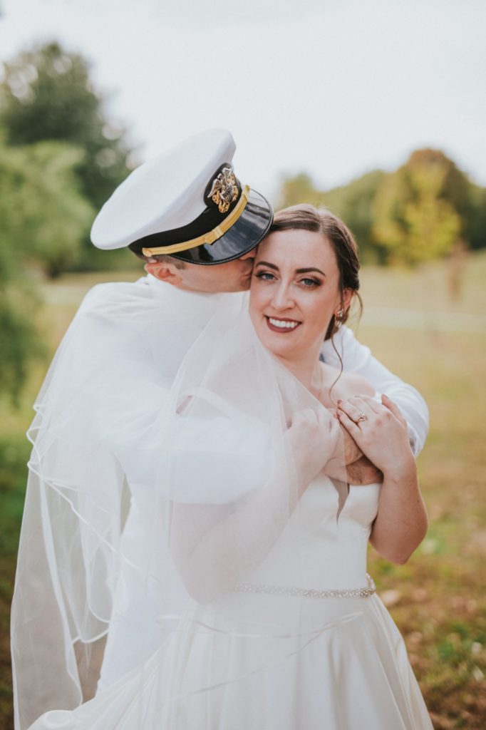 man in naval uniform full dress whites kisses bride on side of head in jackson morrow park
