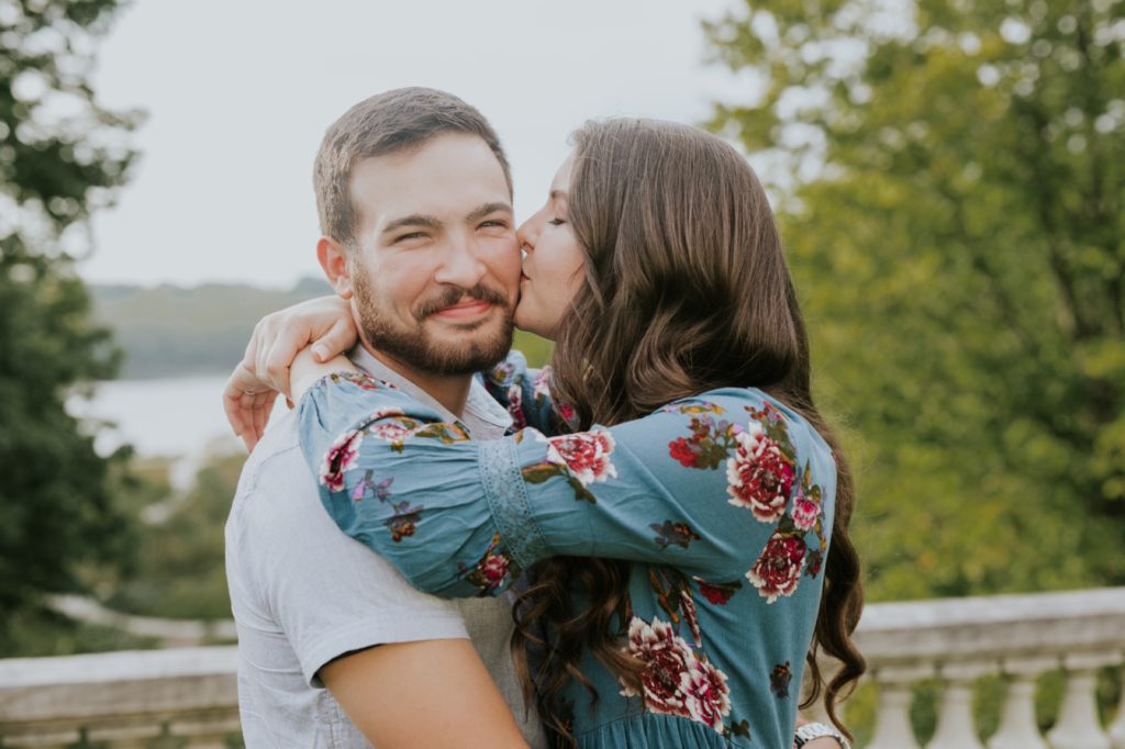 woman in floral dress kisses man in button up shirt on cheek during their IMA engagement session