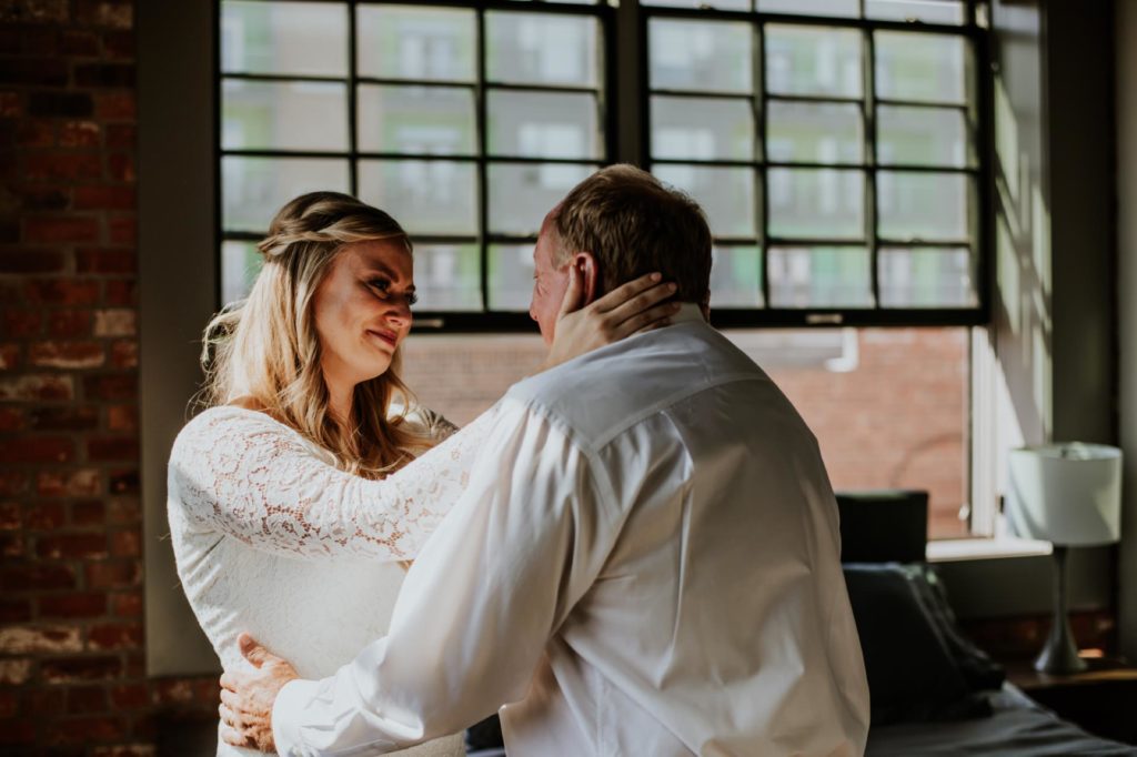 bride holds her dad's head and smiles during first look with dad at blumlux building in indy