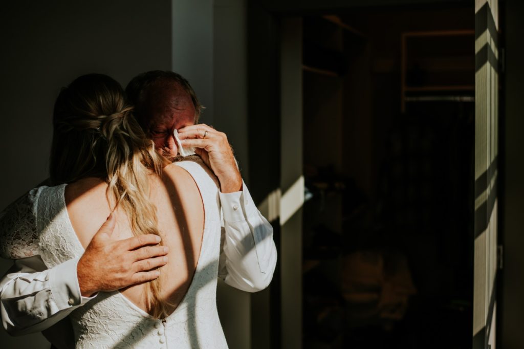 father of the bride cries in moody window light during revealing with his daughter on her wedding day at blumlux buidling in indianapolis