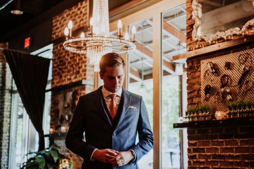 groom in blue suit underneath chandelier in the ball and biscuit