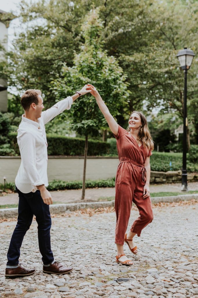 man in white shirt makes arch with hands and arms with woman in orange jumpsuit on historic lockerbie street, one of the Best Indianapolis Engagement Photo Locations