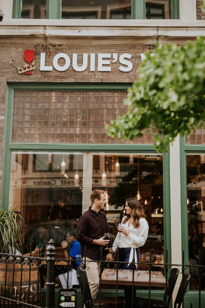man and woman stand in front of Louies Wine Dive for their engagement portraits