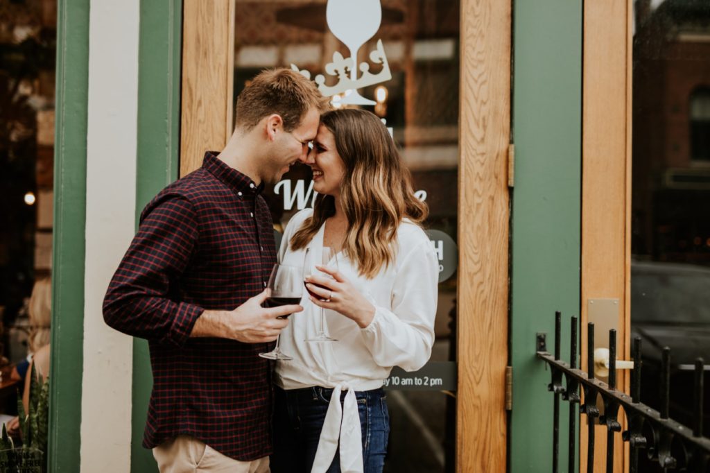 man and woman touch foreheads in front of Louies Wine Dive for their engagement portraits