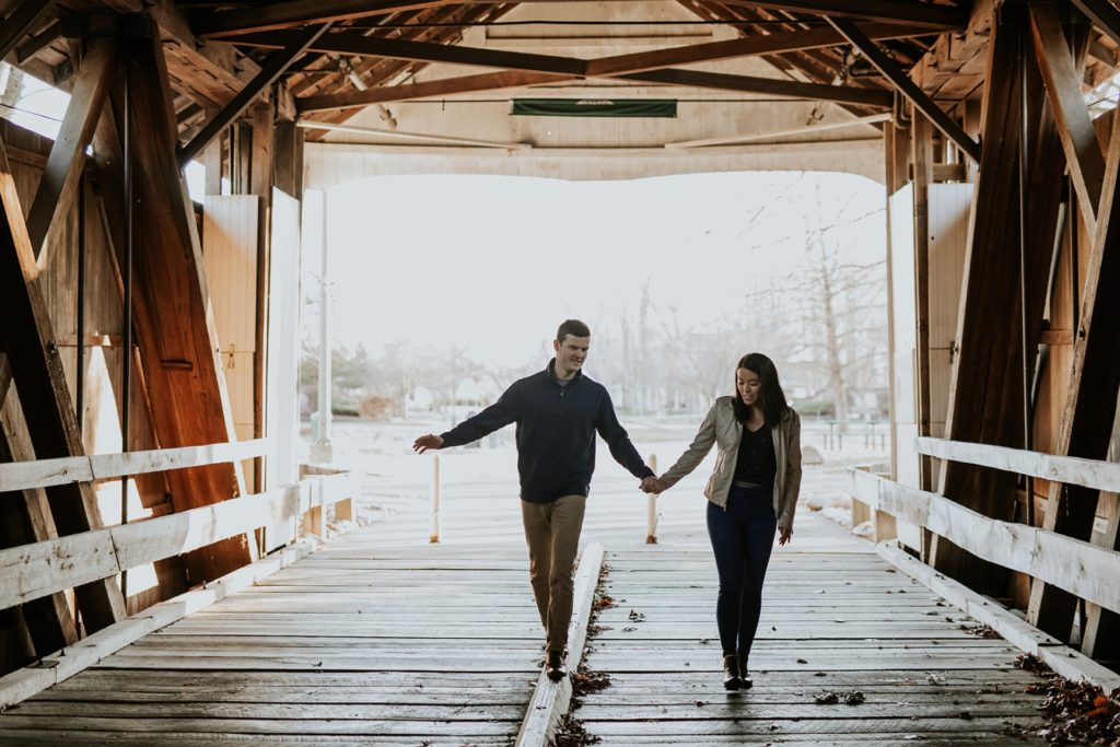 man and woman walk on covered bridge at Potter's Bridge Park, one of the Best Indianapolis Engagement Photo Locations