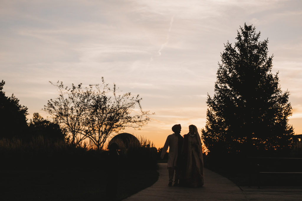 silhouette of man and woman walking at sunset during their Coxhall Gardens wedding