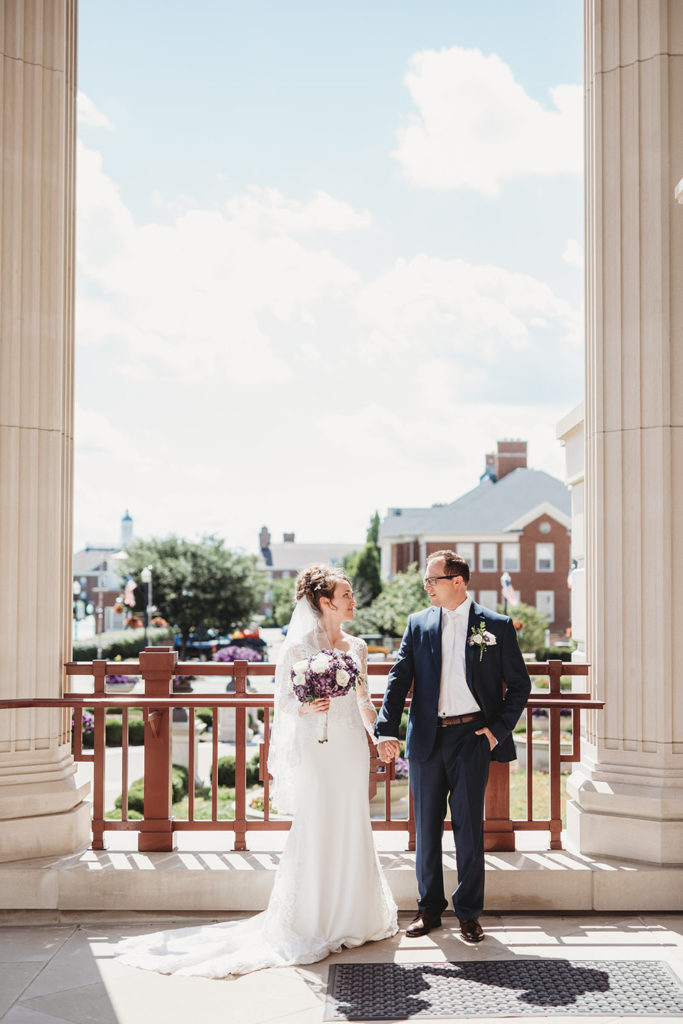 bride and groom stand in shade of the Palladium in Carmel Indiana
