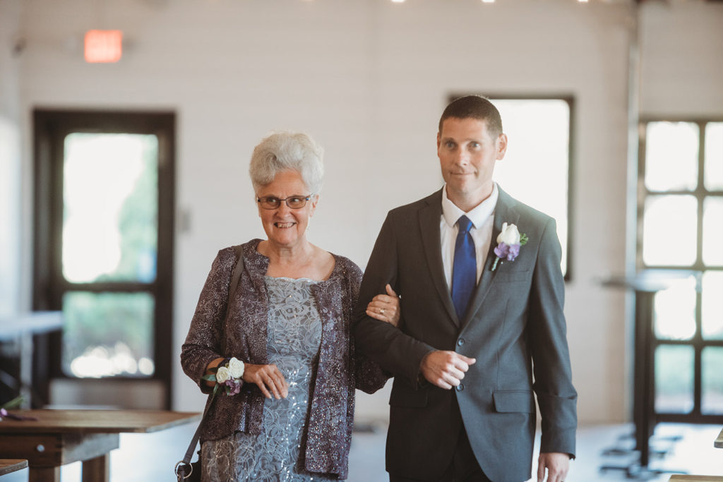 mother of bride walks down aisle with groomsman