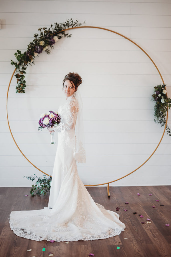 bride in front of wooden circle with floral and a white wall