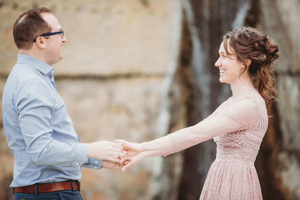 man and woman dance in front of waterfall fountain during during white river park engagement session