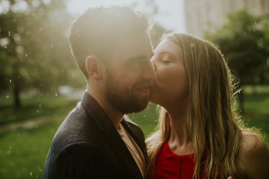 woman kisses man on cheek in rain at indiana statehouse, one of the Best Indianapolis Engagement Photo Locations