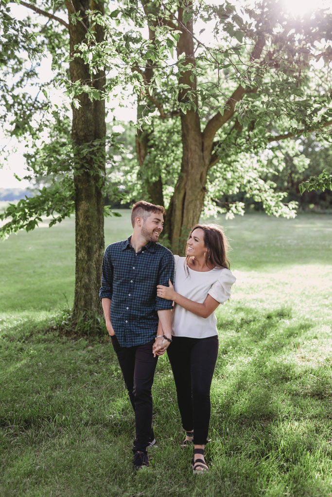 man and woman walk under tree during their noblesville engagement portraits