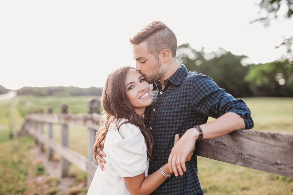 woman snuggles up to man leaning against wooden fence during their hamilton county engagement portraits